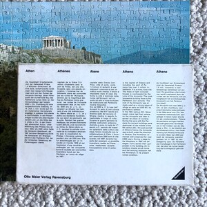K&ouml;nnte beinhalten: Eine Vintage-Postkarte mit einer farbenfrohen Illustration der Akropolis in Athen, Griechenland. Die Postkarte enth&auml;lt Text in mehreren Sprachen &uuml;ber die Geschichte der Akropolis.