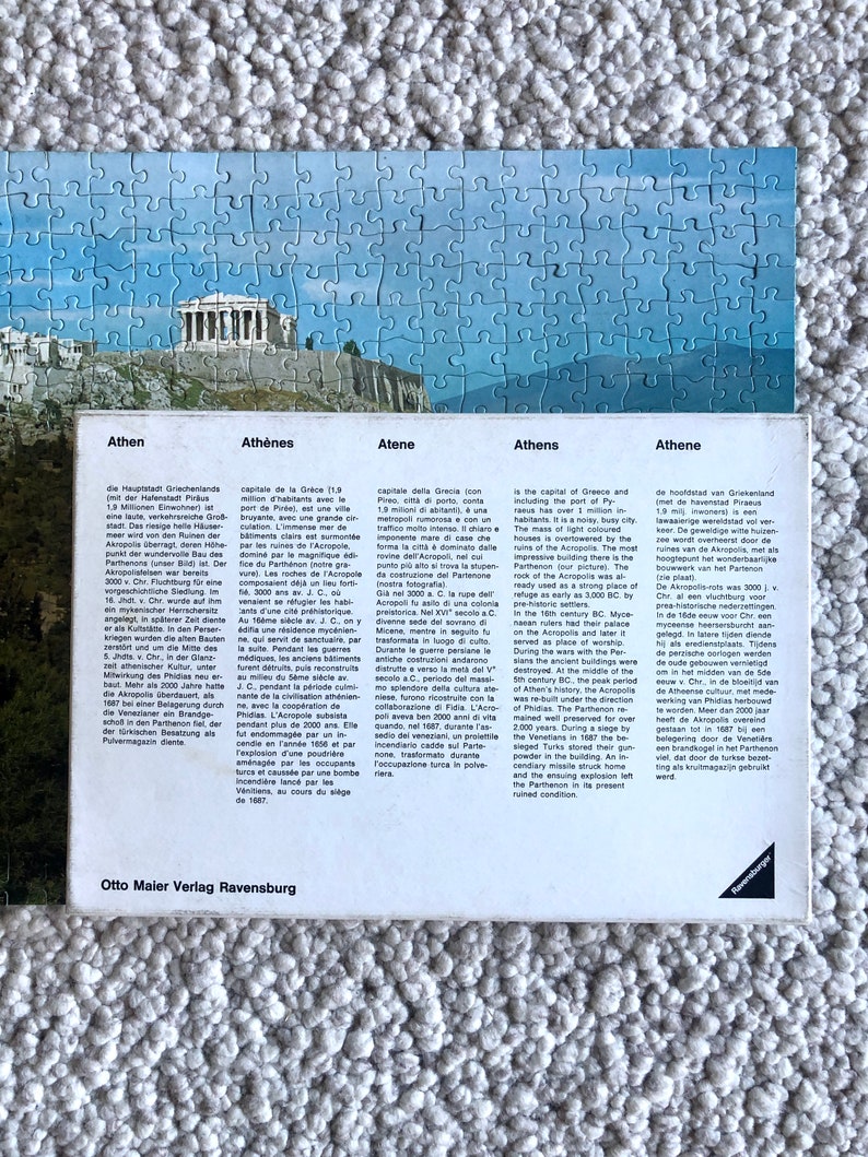 K&ouml;nnte beinhalten: Eine Vintage-Postkarte mit einer farbenfrohen Illustration der Akropolis in Athen, Griechenland. Die Postkarte enth&auml;lt Text in mehreren Sprachen &uuml;ber die Geschichte der Akropolis.