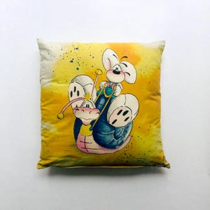 Könnte beinhalten: Quadratisches Zierkissen mit einer Cartoon-Illustration einer Maus, die eine Schnecke reitet. Die Maus trägt eine Latzhose und hält Zügel. Die Schnecke ist blau und rosa, vor einem gelb-orangen Hintergrund im Aquarellstil.