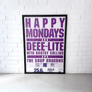 May include: A framed concert poster featuring the text HAPPY MONDAYS AND DEEE-LITE WITH BOOTSY COLLINS AND THE SOUP DRAGONS in bold blue letters with a pink floral pattern. The bottom includes the date 25.6. and the location KÖLN E-WERK.