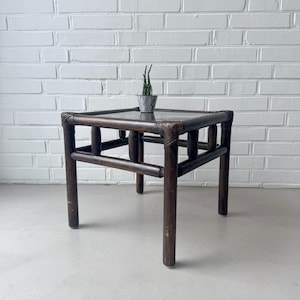 May include: Dark brown square side table with a glass top and a small potted plant. The table has a geometric design and is approximately 20 inches wide and 20 inches long.