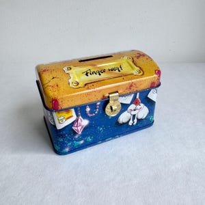 Może przedstawiać: Biały ceramiczny kubek z czarnym uchwytem i napisem "But First, Coffee" czarną, odręczną czcionką. Kubek stoi na białej powierzchni.