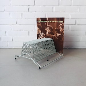 Puede incluir: Un soporte de discos de metal verde claro con un diseño rectangular. El soporte de discos está frente a un álbum de vinilo con el texto "The Smiths The World Won't Listen". La portada del álbum presenta una foto en blanco y negro de personas.