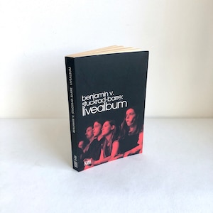 Könnte beinhalten: Ein schwarzes Buch mit einem weißen Titel, der "benjamin v. stuckrad-barre: livealbum" lautet. Das Cover zeigt ein Foto einer Gruppe von Menschen in einem Konzertsetting.