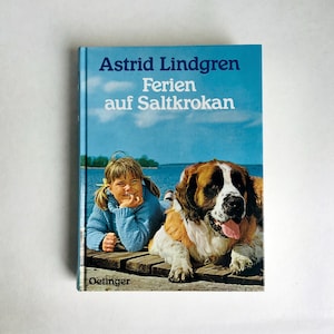 Può includere: Un libro blu con il titolo "Astrid Lindgren Ferien auf Saltkrokan" e un'immagine di una ragazza e un cane su un molo vicino all'acqua.