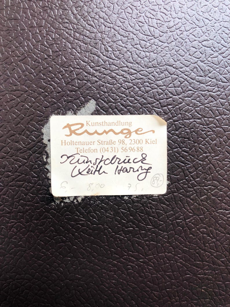 May include: A close-up of a dark brown textured surface with a torn white label. The label features the word "Runge" in a stylized font, along with handwritten text and numbers. The label is slightly torn.