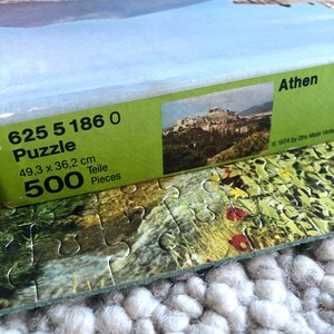 K&ouml;nnte beinhalten: Eine gr&uuml;n-wei&szlig;e Schachtel f&uuml;r ein 500-teiliges Puzzle der Akropolis in Athen, Griechenland. Auf der Schachtel steht der Text "625 5 186 0 Puzzle 49,3 x 36,2 cm 500 Teile Pieces Athen 1974 by Otto Maier Verlag".