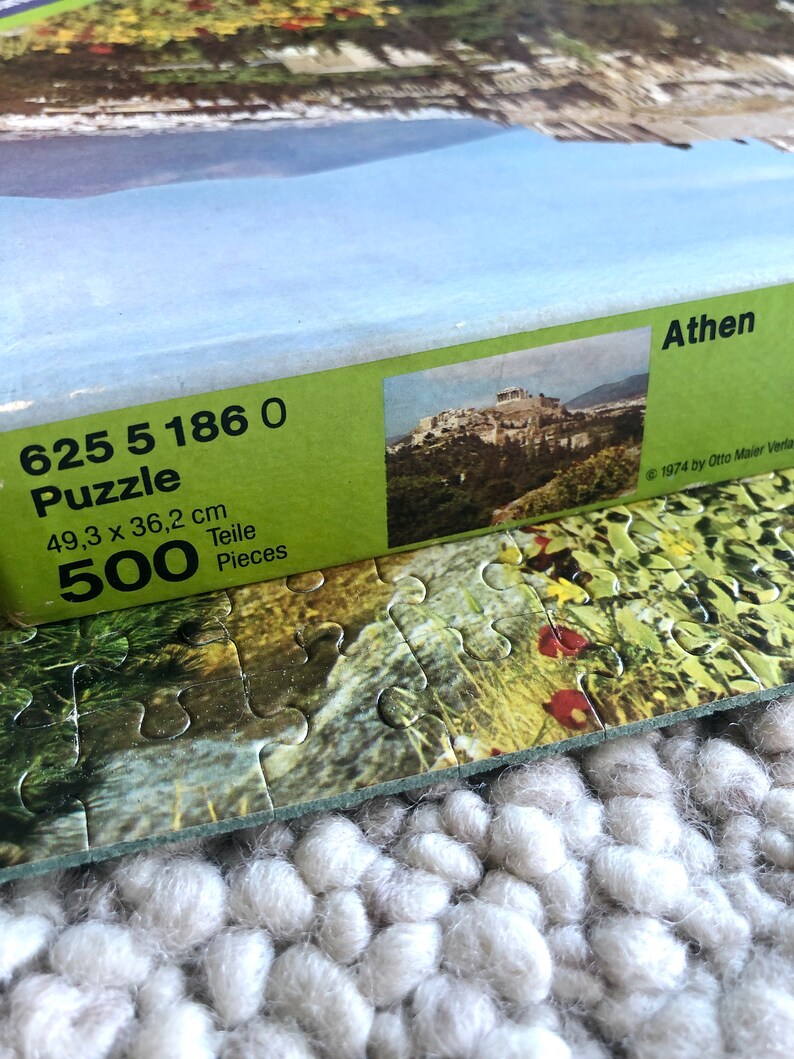 K&ouml;nnte beinhalten: Eine gr&uuml;n-wei&szlig;e Schachtel f&uuml;r ein 500-teiliges Puzzle der Akropolis in Athen, Griechenland. Auf der Schachtel steht der Text "625 5 186 0 Puzzle 49,3 x 36,2 cm 500 Teile Pieces Athen 1974 by Otto Maier Verlag".