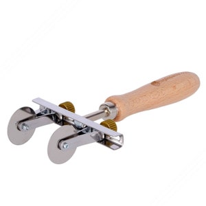 Puede incluir: Un cortador de masa de metal con dos ruedas y un mango de madera. El mango tiene el texto "Vagabond House" en él.