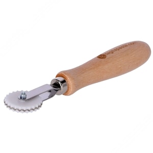 May include: A white plastic pastry wheel with a serrated edge, attached to a silver metal rod and a wooden handle. The handle is engraved with the text "tagliapaste.com".