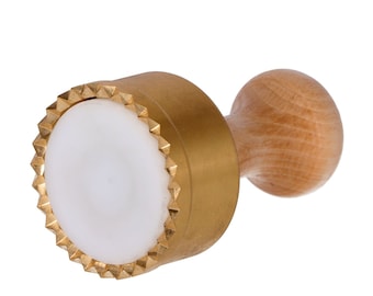 May include: A gold-colored metal cookie cutter with a white plastic center and a wooden handle. The cutter has a scalloped edge.