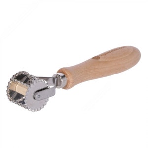 May include: A stainless steel pastry wheel with a wooden handle. The wheel has a serrated edge and a small, round cutter in the center. The handle is made of light brown wood and has the text "Lagostina" printed on it.