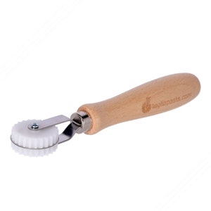 May include: A white plastic pasta cutter with a wooden handle. The handle has the text "tagliapasta.com" printed on it.