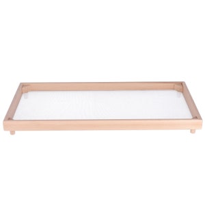 Puede incluir: Un marco de madera con un inserto de malla blanca. El marco es de color marrón claro y tiene una forma rectangular.