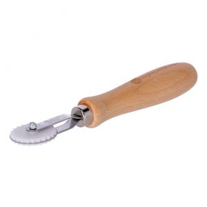 May include: A white and silver rolling cutter with a wooden handle. The cutter has a white wheel with small teeth around the edge.