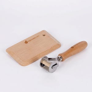 May include: A wooden pasta cutter with a stainless steel blade and a wooden handle, next to a small wooden cutting board. The cutting board has the text tagliapasta.com.