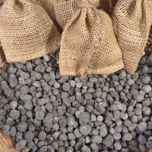May include: A woven basket filled with small, dark gray stones and several burlap sacks tied with twine. The sacks are filled with a light-colored material and are arranged at the top of the basket.