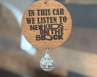 May include: A wooden car air freshener with the text "In this car we listen to New Kids on the Block" and a silver disco ball hanging from it.