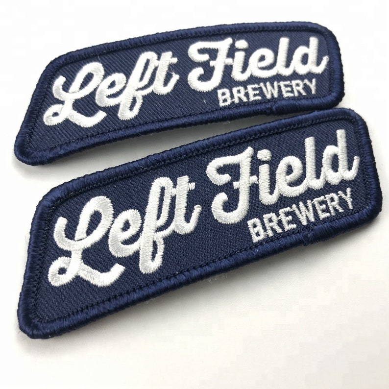 May include: Two navy blue embroidered patches with white stitching. The patches are rectangular and curved at the edges. The text on the patches reads "Left Field Brewery".