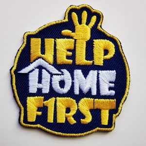 May include: A blue and yellow embroidered patch with the text "Help Home First" and a raised hand.