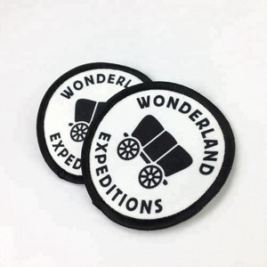 May include: Two white round patches with black borders. The patches have a black wagon illustration and the text "Wonderland Expeditions" in a black circle.