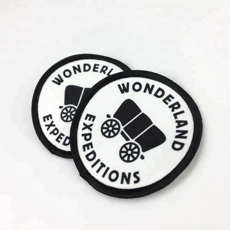 May include: Two white round patches with black borders. The patches have a black wagon illustration and the text "Wonderland Expeditions" in a black circle.