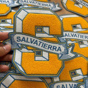 May include: A close-up of a yellow and blue embroidered patch with the number "8" and the text "Salvatierra" in a banner.