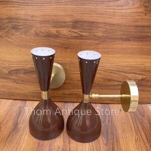 May include: Pair of vintage wall sconces with a mid-century modern design. The sconces feature a brown, bell-shaped shade with a brass accent and a white interior with small dot details. The sconces are mounted on a brass base.
