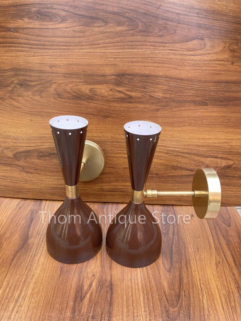 May include: Pair of vintage wall sconces with a mid-century modern design. The sconces feature a brown, bell-shaped shade with a brass accent and a white interior with small dot details. The sconces are mounted on a brass base.