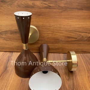 May include: Two brown mid-century modern wall sconces with brass accents. The sconces have a conical shape with a white interior and small circular perforations. The text "Thom Antique Store" is visible.