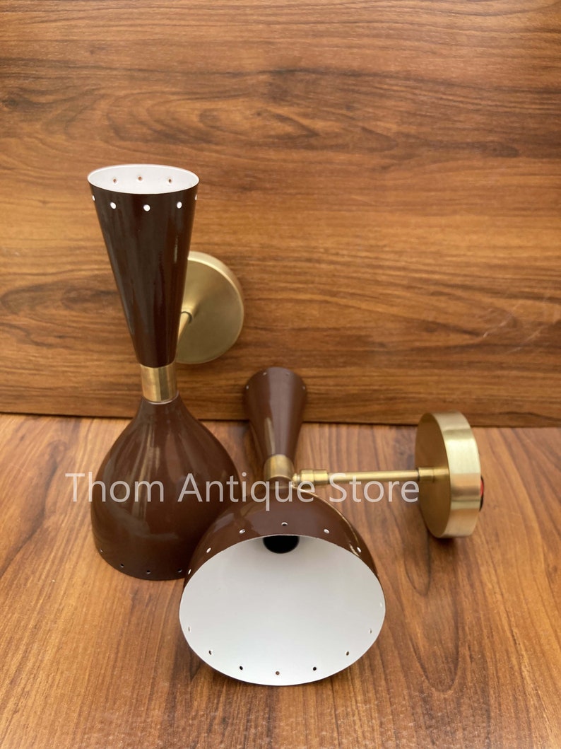May include: Two brown mid-century modern wall sconces with brass accents. The sconces have a conical shape with a white interior and small circular perforations. The text "Thom Antique Store" is visible.