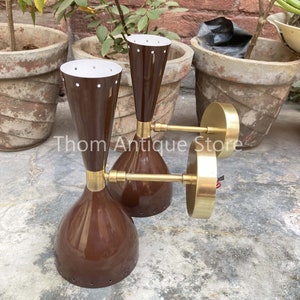 May include: Three vintage brown and brass wall sconces. The sconces have a conical shape with a white interior and small holes near the top. The brass arms extend from the base to the circular wall mount. The sconces are displayed outdoors.