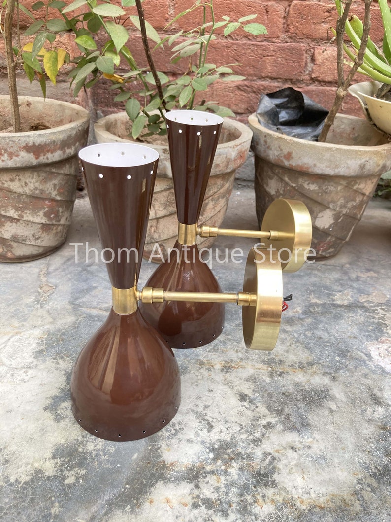 May include: Three vintage brown and brass wall sconces. The sconces have a conical shape with a white interior and small holes near the top. The brass arms extend from the base to the circular wall mount. The sconces are displayed outdoors.