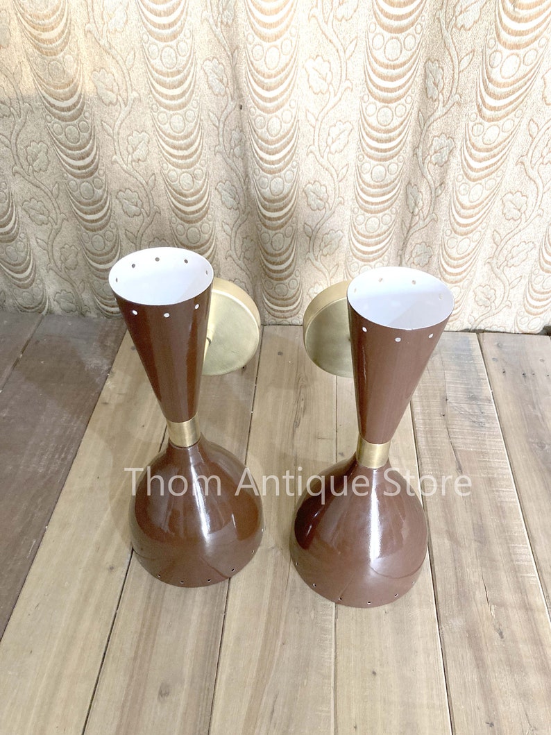 May include: Two vintage brown and brass sconces with a conical shape and white interiors. The sconces have a mid-century modern design, with a round base and a flared top. The text "Thom Antique Store" is visible.