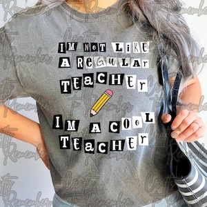 May include: Grey t-shirt with the text "I'M NOT LIKE A REGULAR TEACHER, I'M A COOL TEACHER" in a cut-out style, featuring a yellow pencil with a pink eraser. The shirt is a casual wear item.