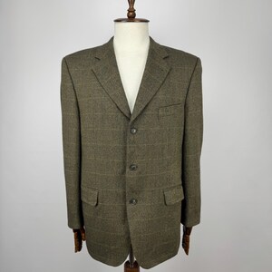 May include: A brown tweed blazer with a subtle plaid pattern. The jacket has a notched lapel, three buttons, and two front pockets. The blazer is displayed on a wooden mannequin.