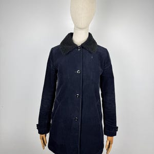 May include: Navy blue corduroy coat with a black faux fur collar. The coat has a button-up front, long sleeves, and a tailored fit. The coat is displayed on a mannequin.