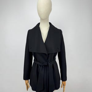 May include: A black coat with a shawl collar and a matching belt tied at the waist. The coat is displayed on a mannequin against a plain white background. The coat has long sleeves and a tailored fit.