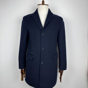 May include: A navy blue overcoat with a notched lapel, three buttons, and two front pockets. The coat is displayed on a wooden mannequin. The coat's length is approximately 40 inches.