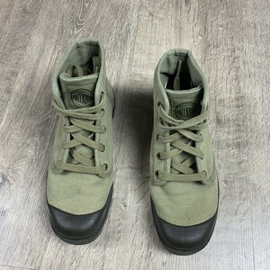 K&ouml;nnte beinhalten: Ein Paar gr&uuml;ne Canvas-High-Top-Sneaker mit schwarzen Schn&uuml;rsenkeln und einer schwarzen Gummisohle. Der Markenname "Palladium" ist auf der Seite jedes Schuhs aufgedruckt.