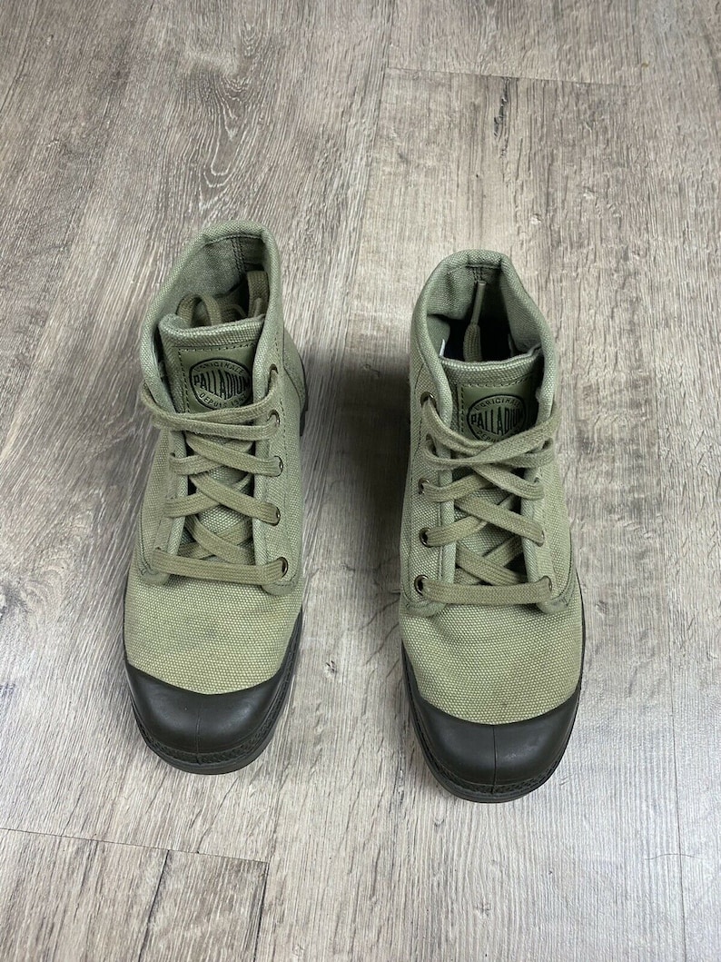 K&ouml;nnte beinhalten: Ein Paar gr&uuml;ne Canvas-High-Top-Sneaker mit schwarzen Schn&uuml;rsenkeln und einer schwarzen Gummisohle. Der Markenname "Palladium" ist auf der Seite jedes Schuhs aufgedruckt.