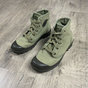 K&ouml;nnte beinhalten: Ein Paar gr&uuml;ne Canvas-Stiefel mit schwarzen Gummisohlen und Schn&uuml;rsenkeln. Die Stiefel haben eine runde Zehenkappe und einen niedrigen Absatz.