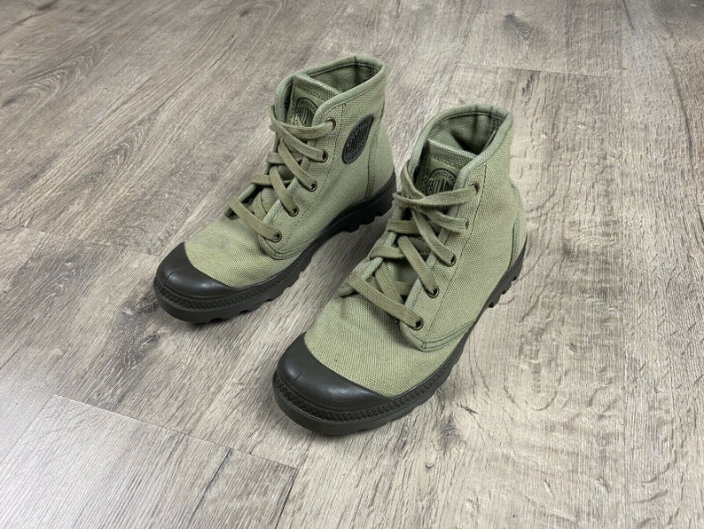 K&ouml;nnte beinhalten: Ein Paar gr&uuml;ne Canvas-Stiefel mit schwarzen Gummisohlen und Schn&uuml;rsenkeln. Die Stiefel haben eine runde Zehenkappe und einen niedrigen Absatz.