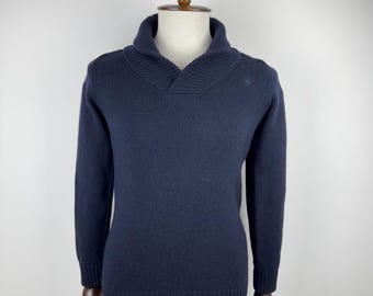 Könnte beinhalten: Ein marineblauer Pullover mit Schalkragen und langen Ärmeln. Der Pullover wird auf einer Holzpuppe präsentiert. Der Kragen ist umgeschlagen und die Ärmel reichen bis zu den hölzernen Händen der Puppe. Der Pullover hat einen gerippten Saum und Bündchen.