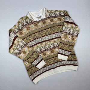 May include: A collared sweater with a cream-colored collar and cuffs. The sweater features a repeating pattern of floral and geometric designs in shades of brown, green, and cream. The sweater is made of a soft, knitted material.