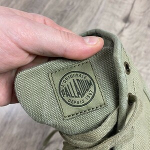 K&ouml;nnte beinhalten: Nahaufnahme eines gr&uuml;nen Canvas-Schuhs mit einem schwarz-wei&szlig;en Logo, auf dem "Original Palladium Depuis 1947" steht.