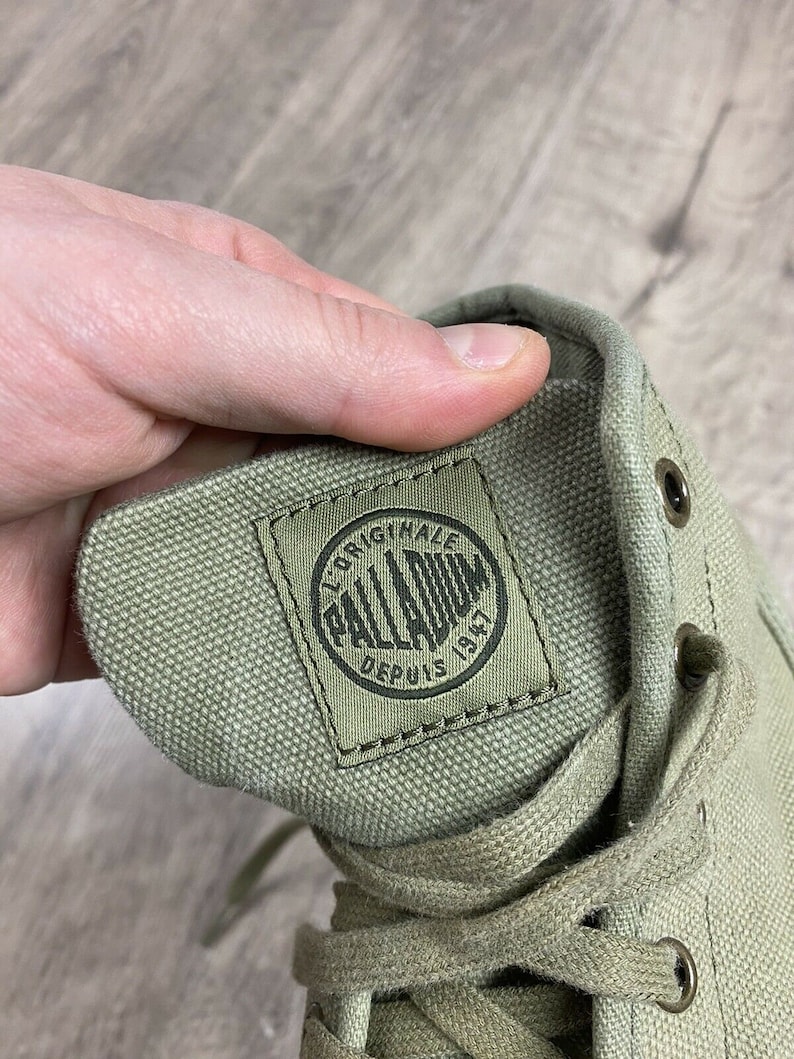 K&ouml;nnte beinhalten: Nahaufnahme eines gr&uuml;nen Canvas-Schuhs mit einem schwarz-wei&szlig;en Logo, auf dem "Original Palladium Depuis 1947" steht.