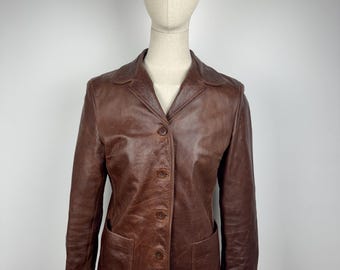 May include: A brown leather blazer with a classic design. The jacket features a notched collar, button closure, and two front pockets. The blazer is displayed on a mannequin. The leather has a slightly worn appearance.
