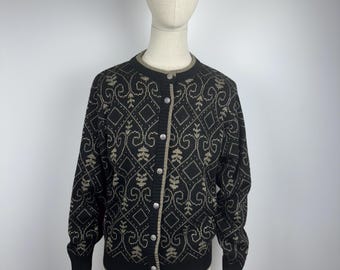 May include: Black cardigan with a geometric pattern in tan and cream. The sweater has a round neckline, long sleeves, and a button-down front. The trim and buttons are silver. The garment is displayed on a mannequin.