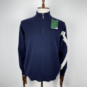 Peut inclure: Un pull bleu marine avec une bande diagonale blanche sur la manche droite. Le pull a une fermeture éclair à moitié et un col montant. Le pull porte une étiquette indiquant "Scott & Charters".